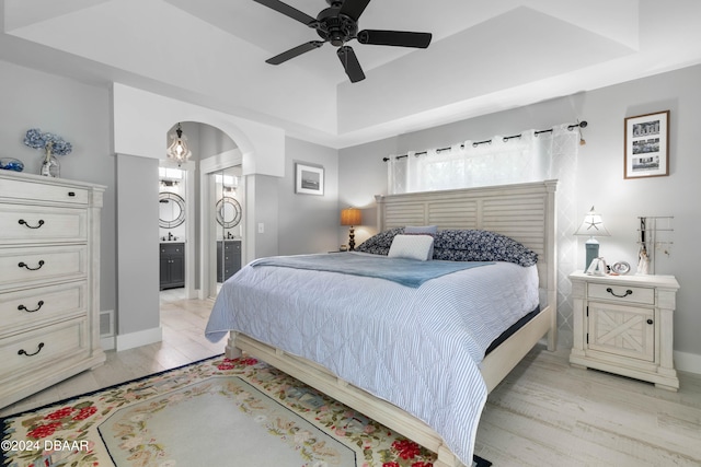 bedroom featuring ensuite bathroom, ceiling fan, a raised ceiling, and light wood-type flooring