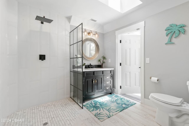 bathroom featuring vanity, a skylight, toilet, a tile shower, and wood-type flooring