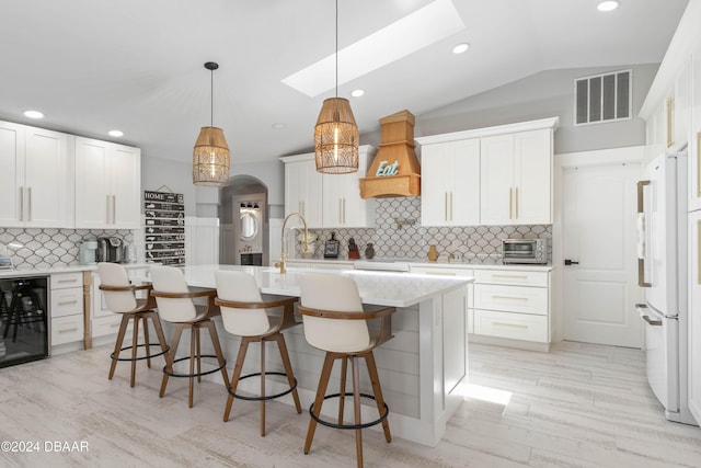 kitchen with decorative backsplash, white cabinetry, premium range hood, and beverage cooler