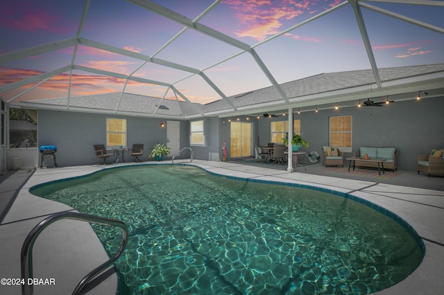 pool at dusk featuring outdoor lounge area, a patio, glass enclosure, and ceiling fan