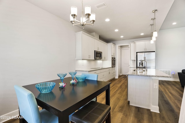 kitchen featuring a kitchen island with sink, dark hardwood / wood-style floors, white cabinetry, appliances with stainless steel finishes, and decorative light fixtures