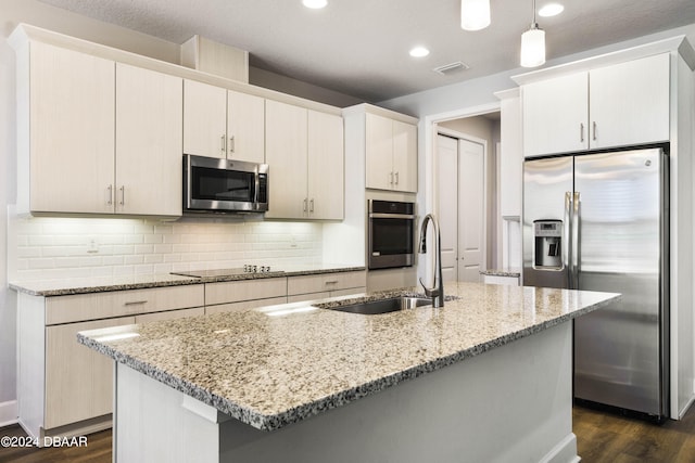 kitchen with light stone counters, appliances with stainless steel finishes, dark hardwood / wood-style floors, pendant lighting, and an island with sink