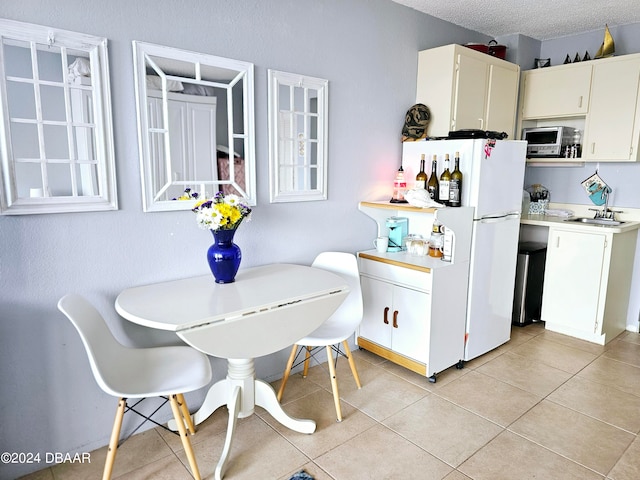 kitchen with a textured ceiling, sink, light tile patterned floors, white fridge, and white cabinetry