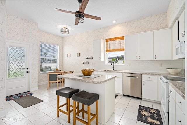 kitchen featuring white cabinets, a wealth of natural light, a center island, and white appliances