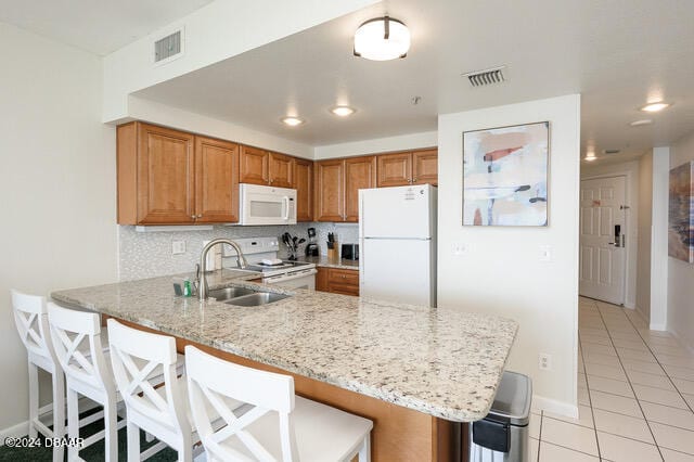 kitchen featuring kitchen peninsula, a kitchen breakfast bar, white appliances, and sink