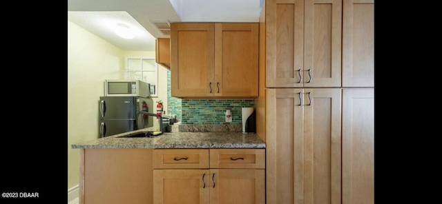 kitchen featuring refrigerator, backsplash, sink, and light stone countertops