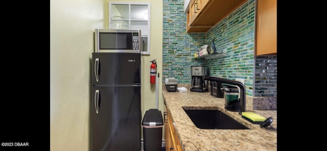 kitchen featuring light stone countertops, black fridge, sink, and tasteful backsplash