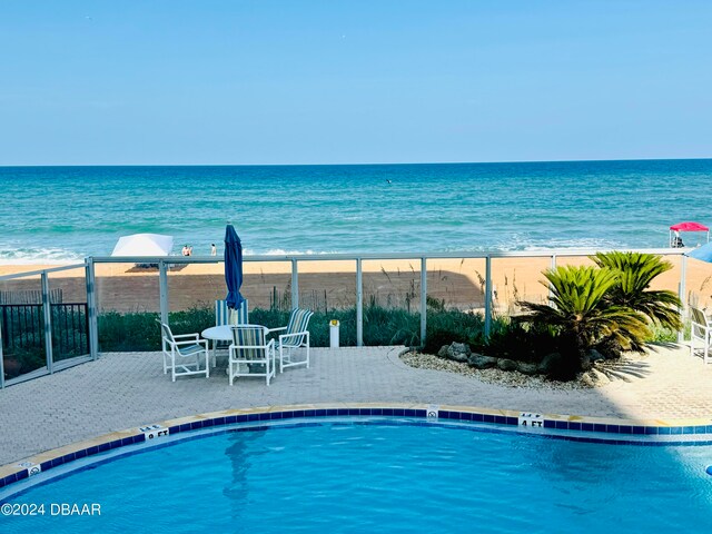 view of swimming pool featuring a view of the beach, a water view, and a patio