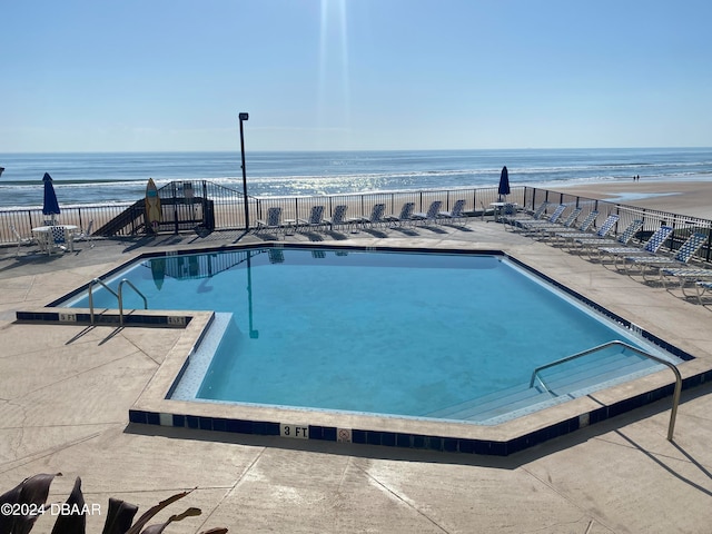 view of swimming pool with a beach view, a water view, and a patio area