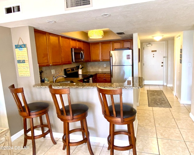 kitchen featuring stainless steel appliances, a breakfast bar area, light stone counters, and kitchen peninsula