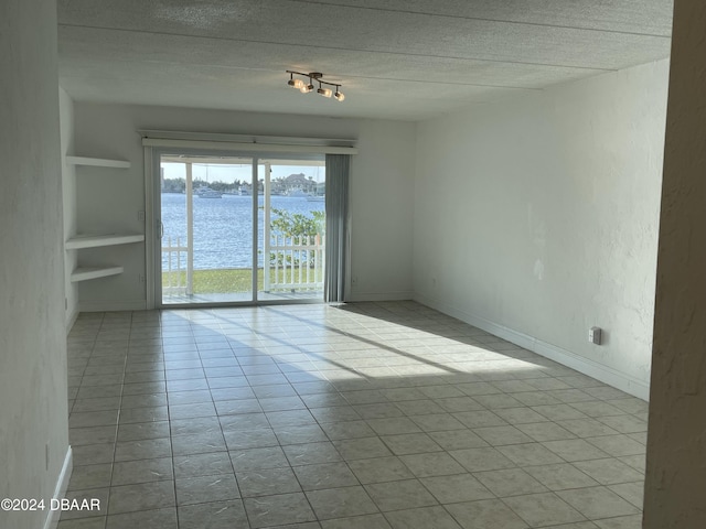 spare room featuring light tile patterned floors, built in features, a textured ceiling, and a water view