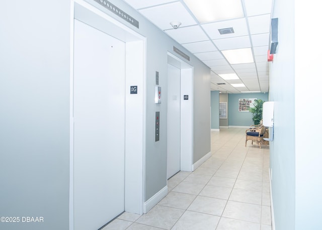 hallway featuring a paneled ceiling, elevator, and light tile patterned floors