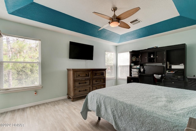 bedroom with a tray ceiling, multiple windows, light hardwood / wood-style floors, and ceiling fan