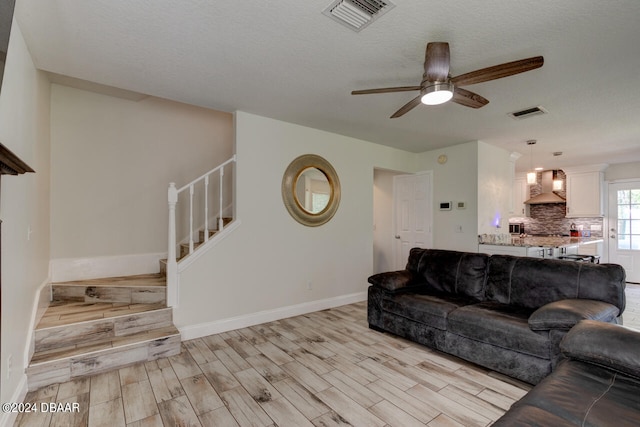 living room with ceiling fan, light hardwood / wood-style floors, and a textured ceiling