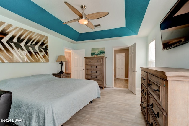 bedroom with a raised ceiling, ceiling fan, and light hardwood / wood-style floors