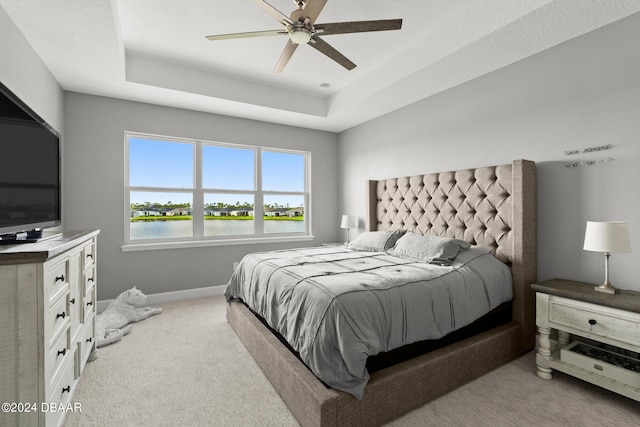 bedroom with ceiling fan, a raised ceiling, a water view, and light colored carpet