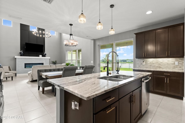 kitchen with dark brown cabinetry, sink, light stone counters, decorative light fixtures, and a kitchen island with sink