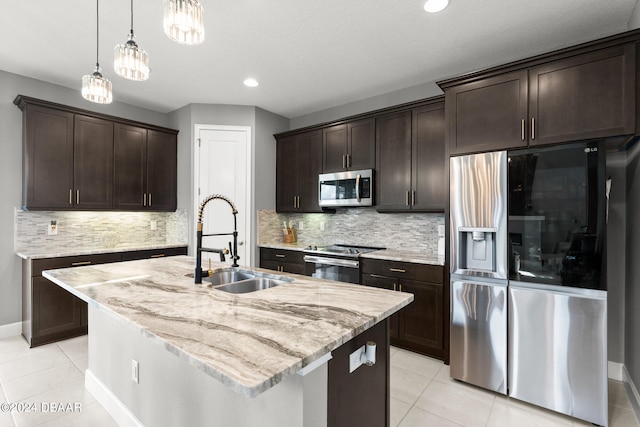 kitchen featuring stainless steel appliances, backsplash, dark brown cabinetry, sink, and an island with sink