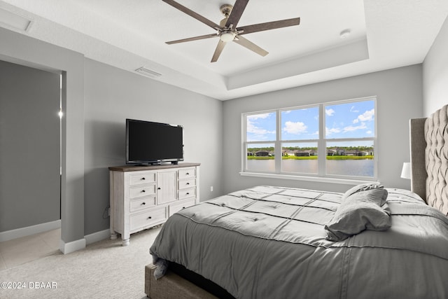 carpeted bedroom featuring a tray ceiling and ceiling fan