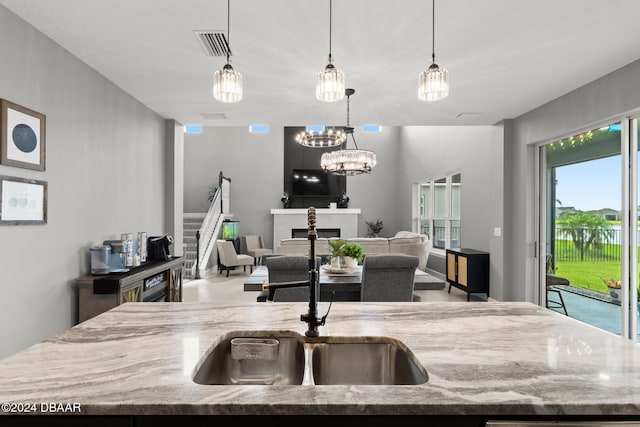 kitchen featuring a fireplace, hanging light fixtures, light stone counters, and a kitchen island with sink