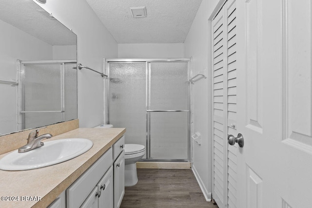 bathroom featuring wood-type flooring, toilet, a textured ceiling, an enclosed shower, and vanity