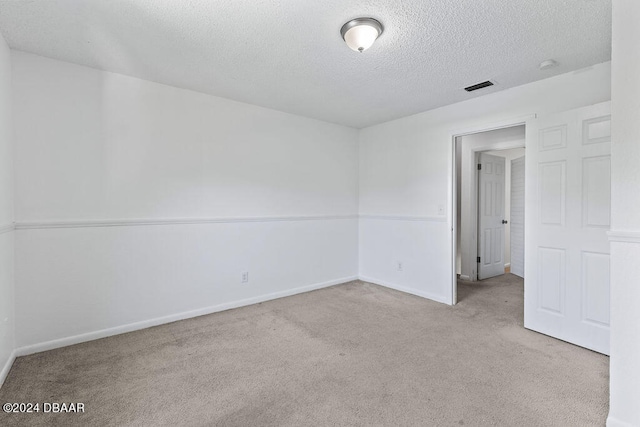 spare room with light colored carpet and a textured ceiling