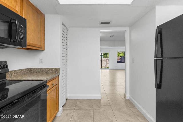 kitchen with dark stone counters, light tile patterned floors, and black appliances