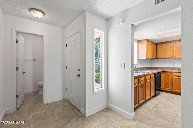 kitchen with light tile patterned floors, a textured ceiling, sink, and dishwasher