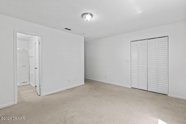 unfurnished bedroom with connected bathroom, light carpet, a textured ceiling, and a closet