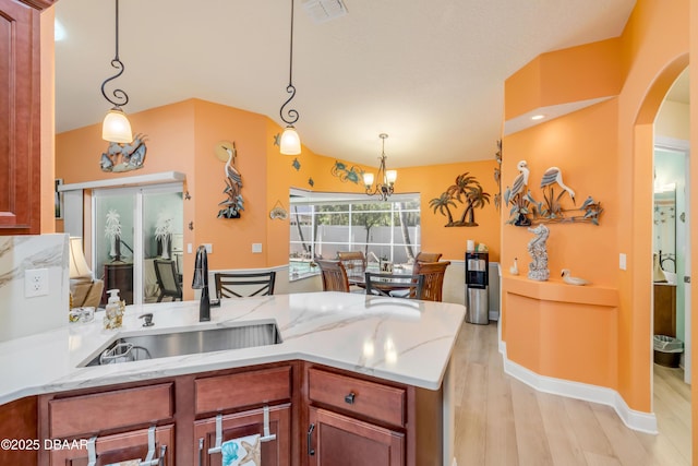 406 Phillips Creek Ln, New Smyrna Beach, FL 32168 - kitchen featuring light wood-type flooring, light stone countertops, a peninsula, hanging light fixtures, and arched walkways