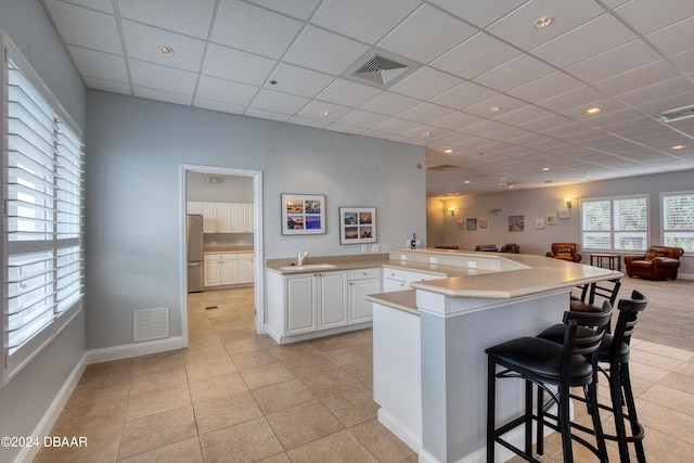 kitchen featuring a kitchen breakfast bar, sink, light tile patterned floors, white cabinetry, and stainless steel refrigerator