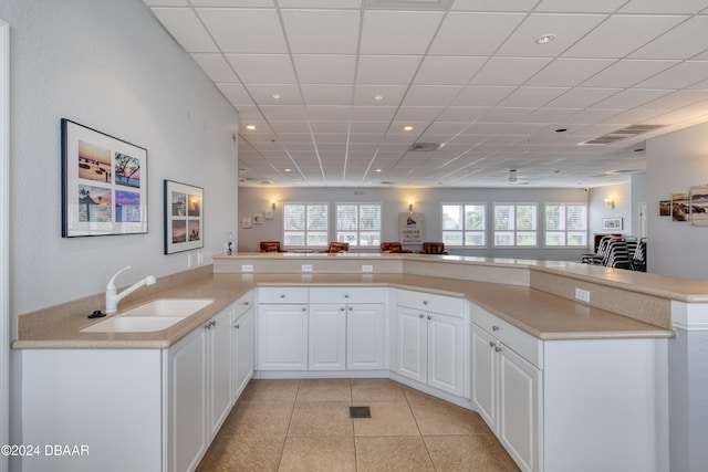 kitchen with white cabinetry, light tile patterned flooring, kitchen peninsula, and sink