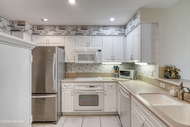 kitchen with white cabinets, light tile patterned floors, white appliances, and sink