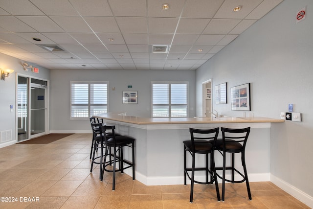 kitchen with a kitchen bar, light tile patterned floors, kitchen peninsula, and a drop ceiling