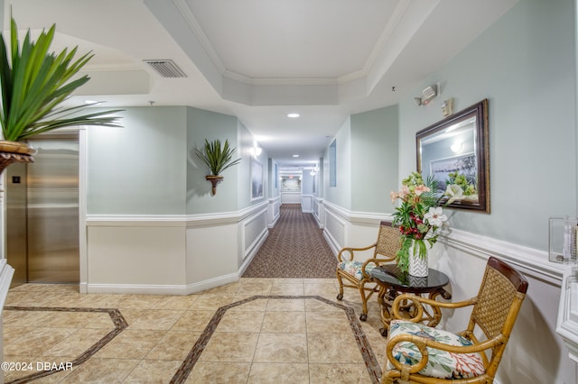 hall featuring light tile patterned flooring, a raised ceiling, crown molding, and elevator