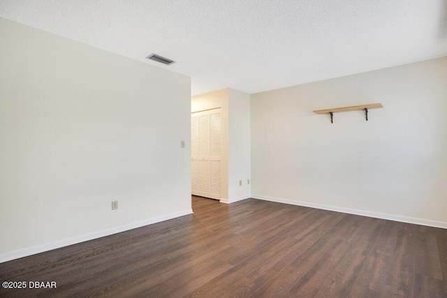 unfurnished room featuring dark wood-type flooring, visible vents, a textured ceiling, and baseboards