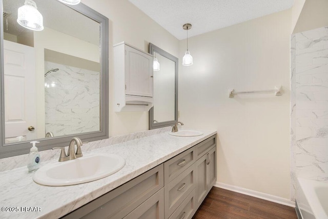 full bath with double vanity, a sink, a textured ceiling, and wood finished floors