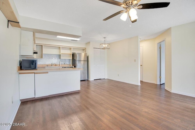 kitchen featuring black microwave, a peninsula, wood finished floors, freestanding refrigerator, and decorative backsplash