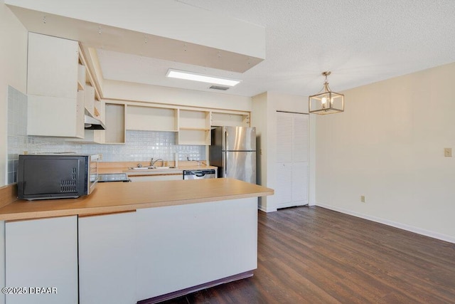 kitchen featuring light countertops, freestanding refrigerator, a sink, black microwave, and a peninsula