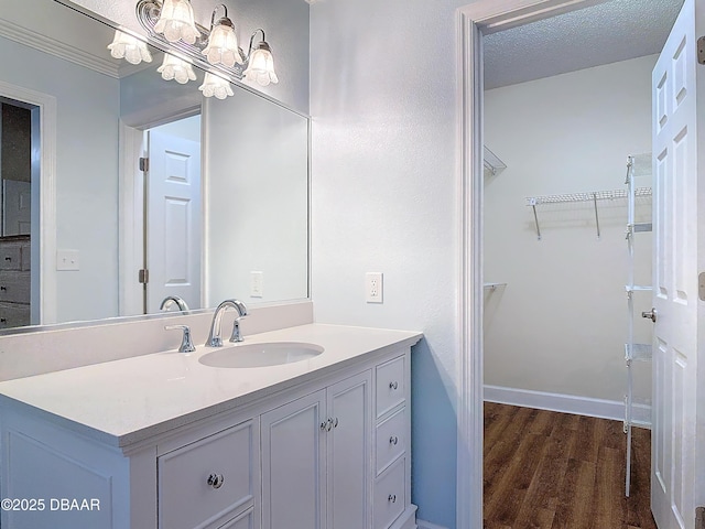 bathroom with a spacious closet, a textured ceiling, vanity, wood finished floors, and baseboards