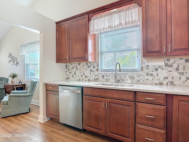 kitchen with tasteful backsplash, light wood-style flooring, light countertops, stainless steel dishwasher, and a sink