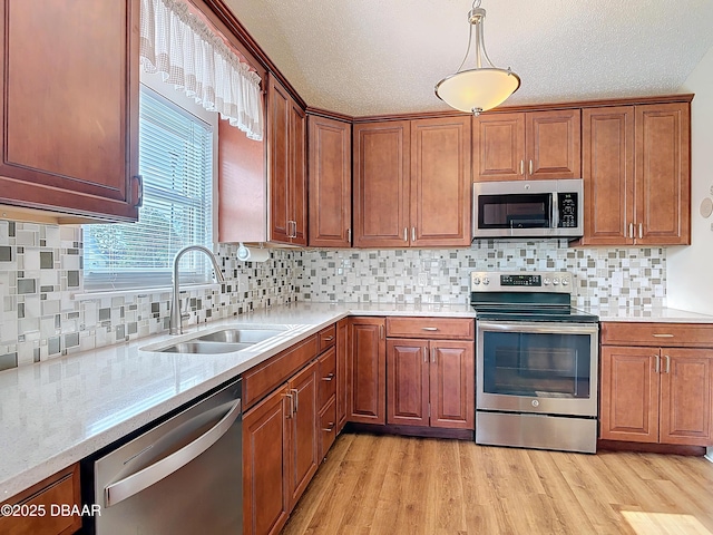 kitchen with stainless steel appliances, a sink, light wood-style flooring, and brown cabinets