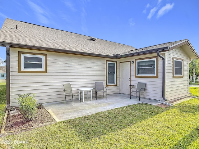 rear view of property with a yard, a shingled roof, and a patio