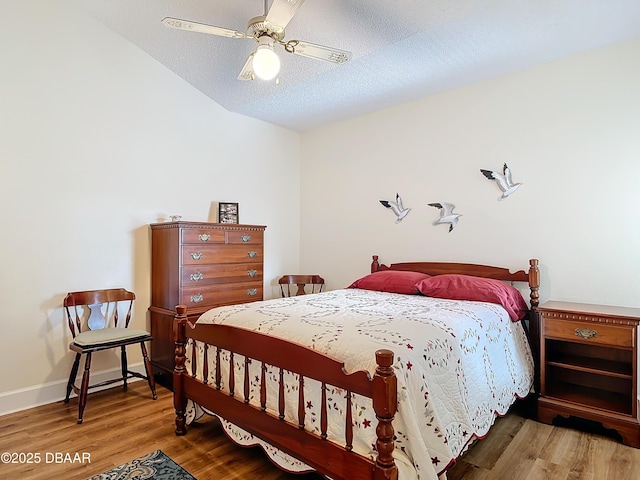 bedroom with a textured ceiling, lofted ceiling, wood finished floors, a ceiling fan, and baseboards