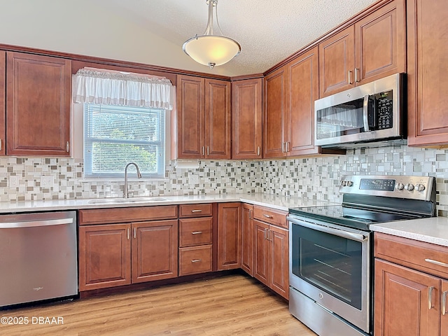 kitchen featuring brown cabinets, stainless steel appliances, light countertops, light wood-style floors, and a sink