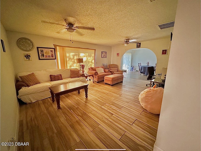 living room featuring light hardwood / wood-style floors, ceiling fan, and a textured ceiling