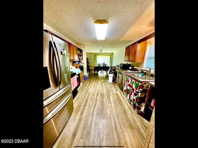 kitchen with a textured ceiling, appliances with stainless steel finishes, light hardwood / wood-style floors, and sink