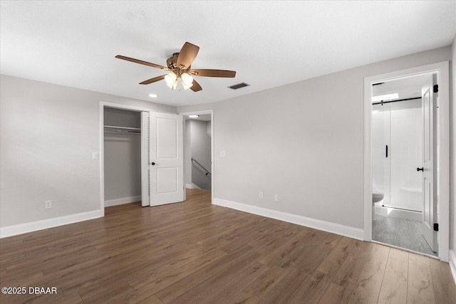 unfurnished bedroom featuring baseboards, visible vents, ensuite bath, dark wood-type flooring, and a closet