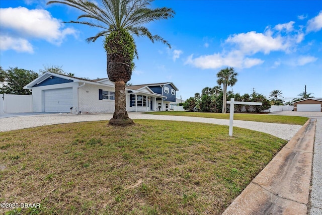 view of front facade featuring gravel driveway, brick siding, an attached garage, a front yard, and fence