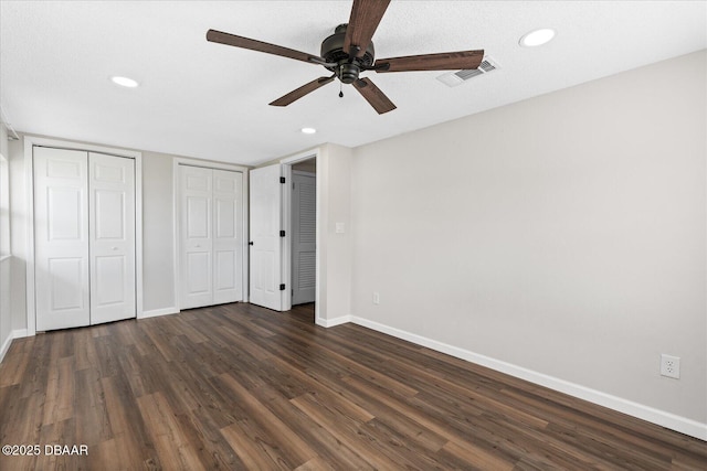 unfurnished bedroom featuring baseboards, visible vents, dark wood-style flooring, two closets, and recessed lighting